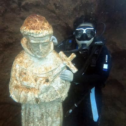 Diver alongside submerged statue holding a cross at depth