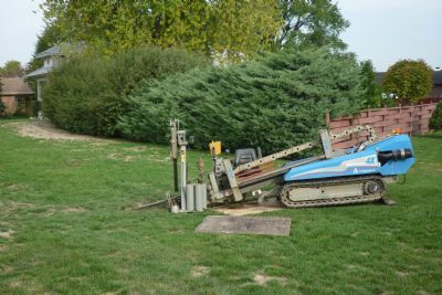 Compact track-mounted directional boring machine positioned on a residential lawn with drill rod in the ground