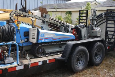 Horizontal directional drilling rig loaded and strapped onto an equipment trailer with drill rods staged beside it