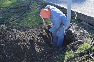 Field technician working at the base of a parking lot light pole with exposed conduit and hand tools