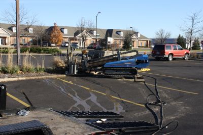Directional drilling rig set up on an active commercial asphalt parking lot with drill rods staged nearby