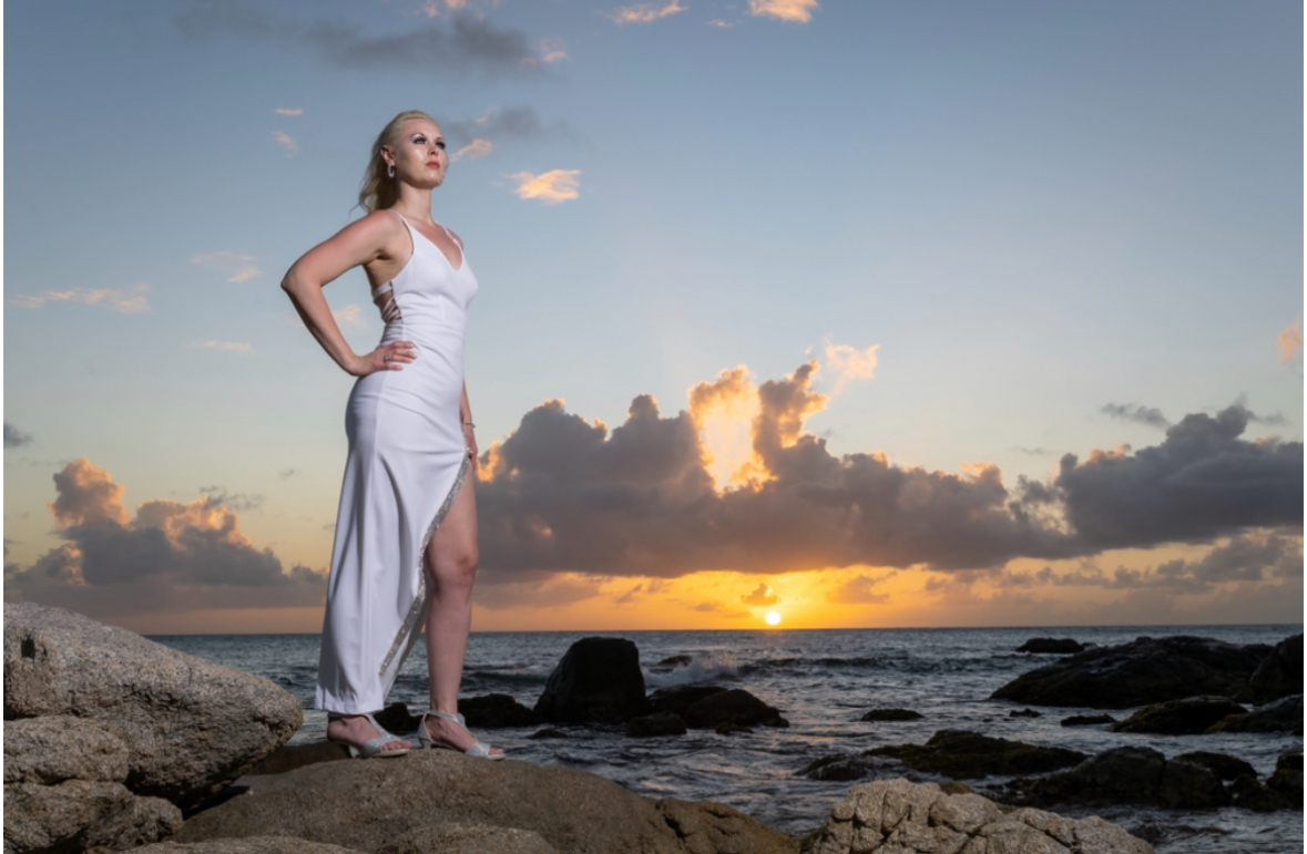 Jodi Lynn Pavlock standing resilient on coastal ocean rocks at golden hour sunset.
