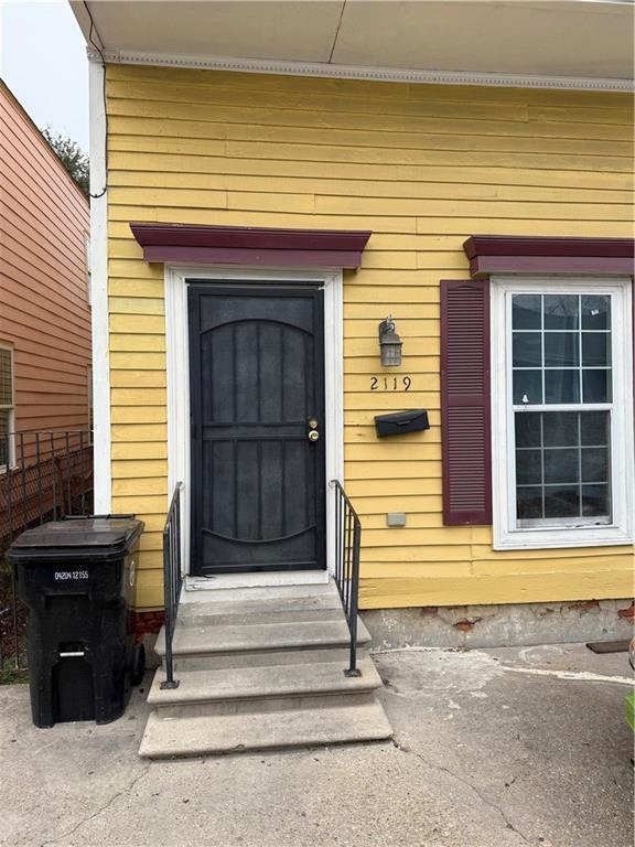 Exterior photograph of 2119 N. Villere Street showing yellow clapboard facade, burgundy trim, and front entryway
