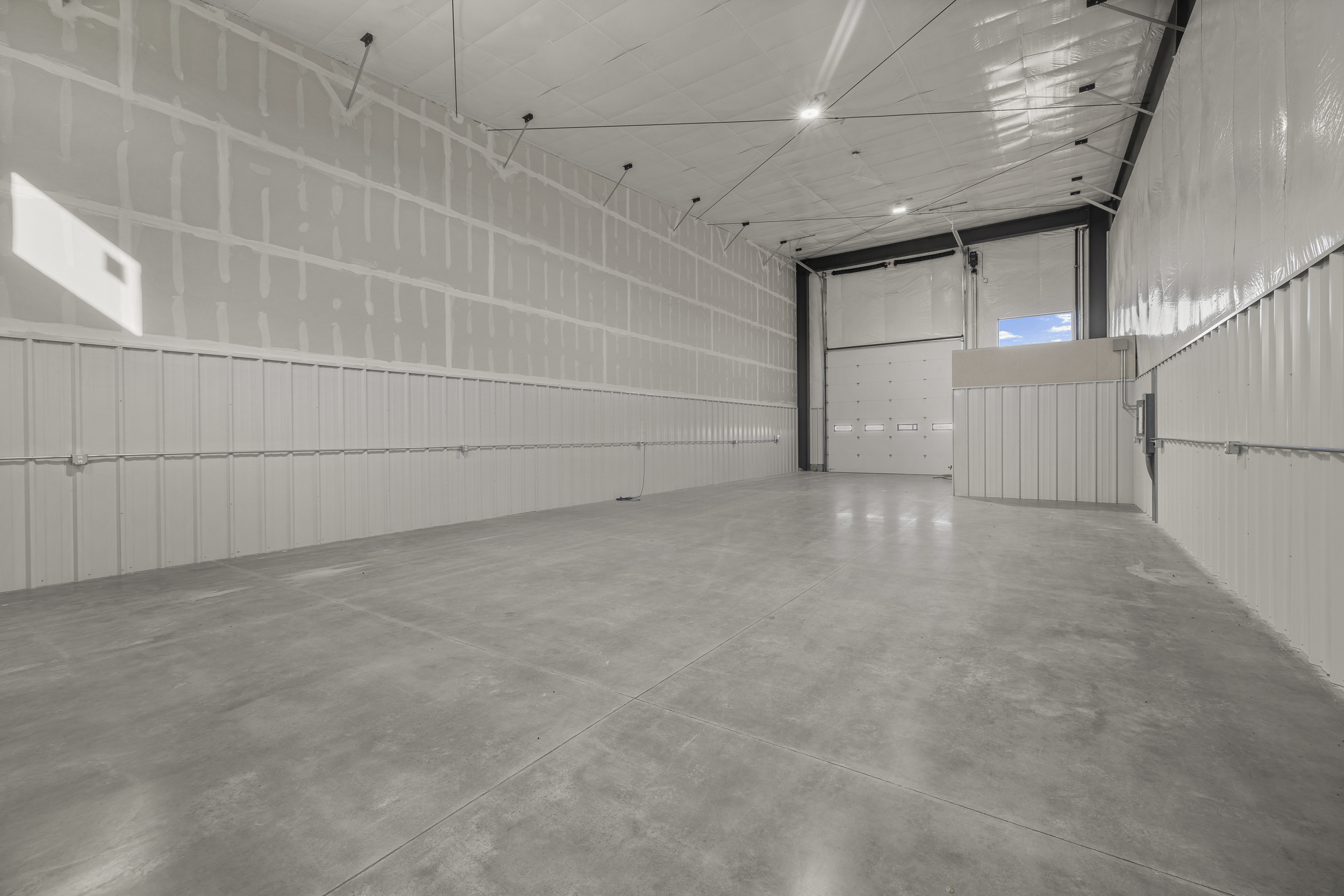 Spacious warehouse bay floor with sealed concrete, insulated ceiling, and drive-in semi-accessible roll-up door