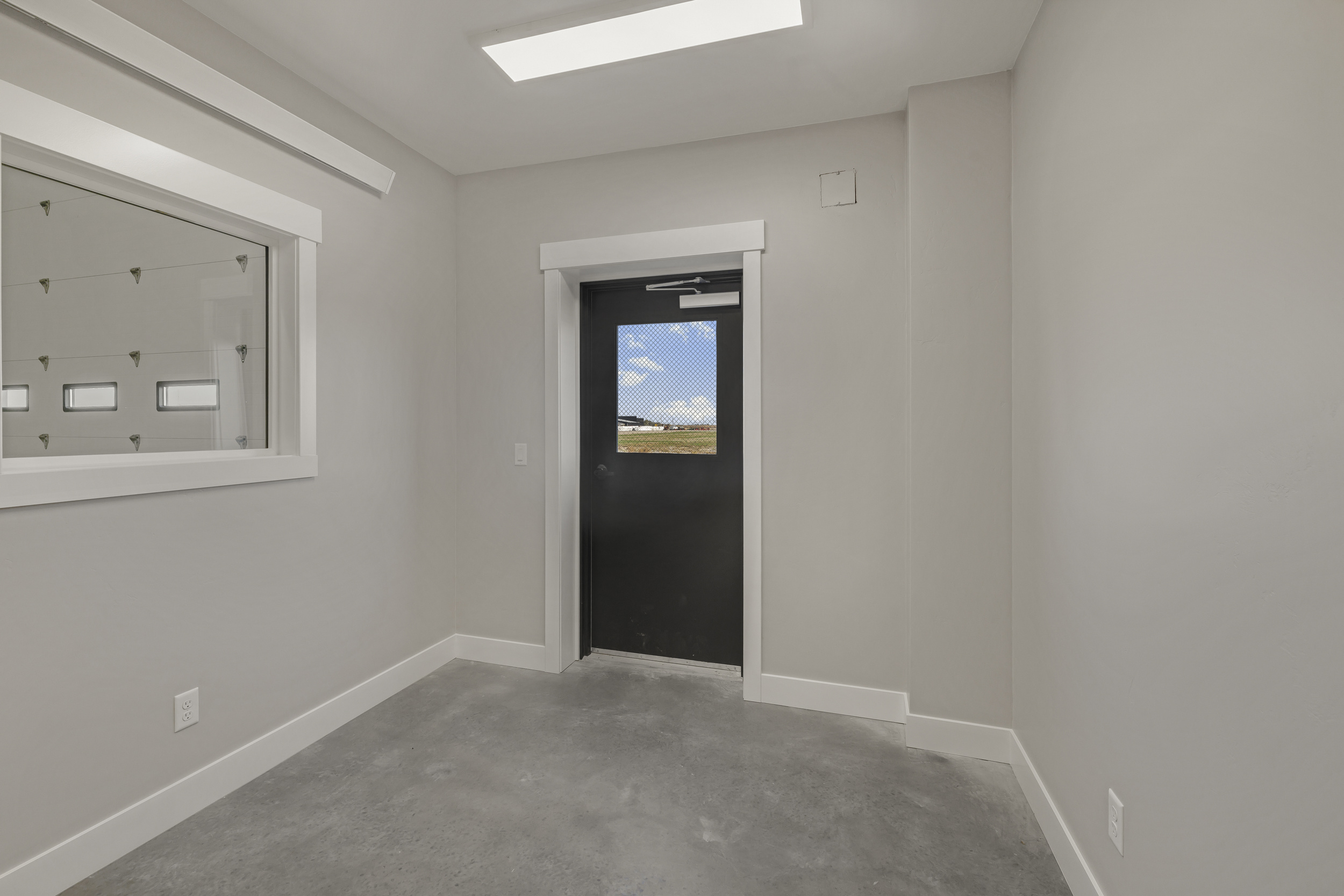 Finished private office inside shop bay with sealed concrete floor, daylight window, and entry door