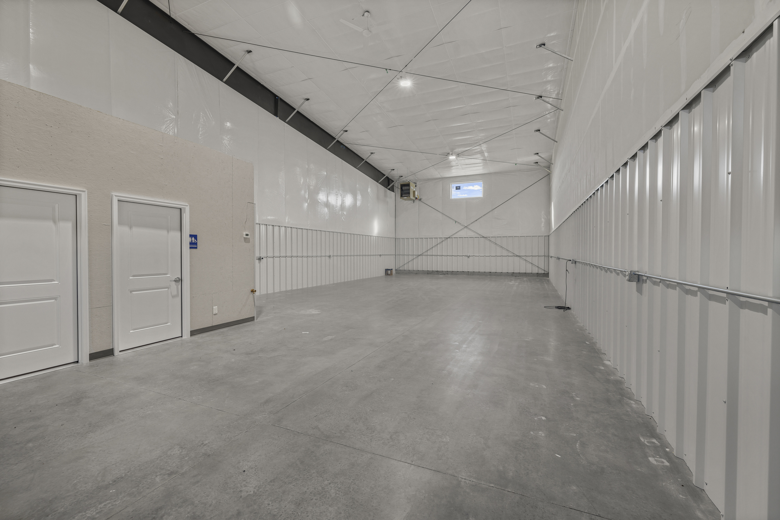 Interior of 2,100 sq ft shop bay with tall ceilings, sealed concrete floors, white metal wall panels, and private office entry