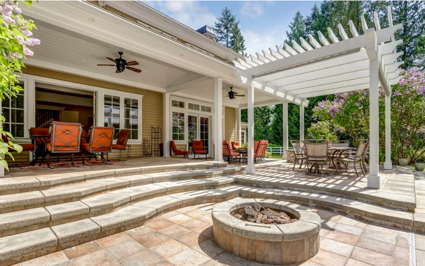 Custom stone patio, fire pit, and white pergola installation