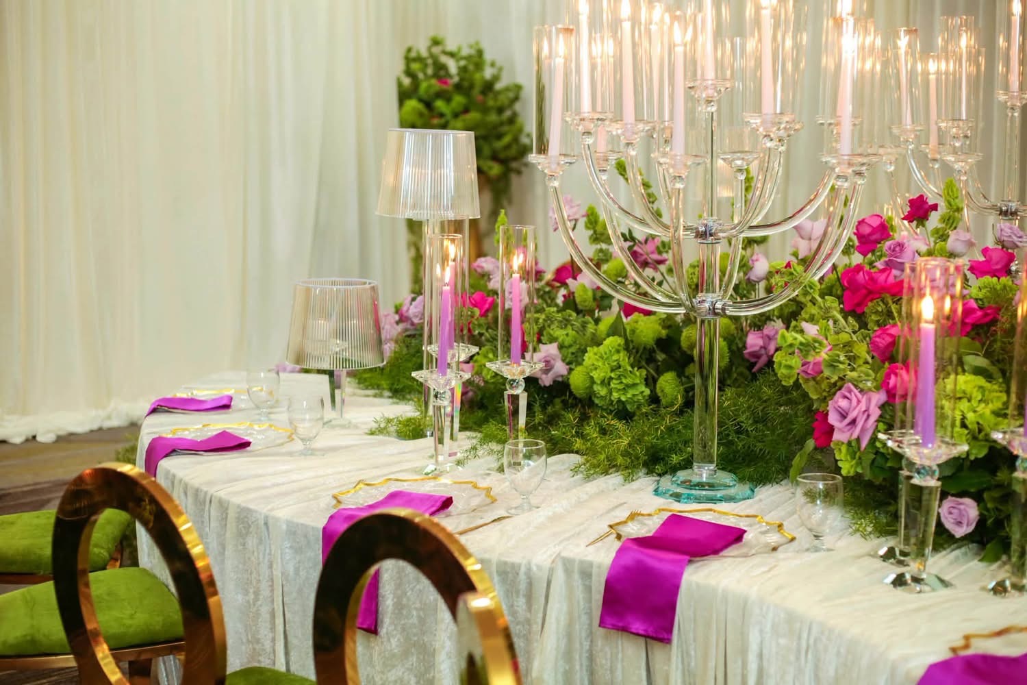 Close-up of luxury reception table with glowing taper candles in crystal candelabras, purple satin napkins, and rich floral centerpiece