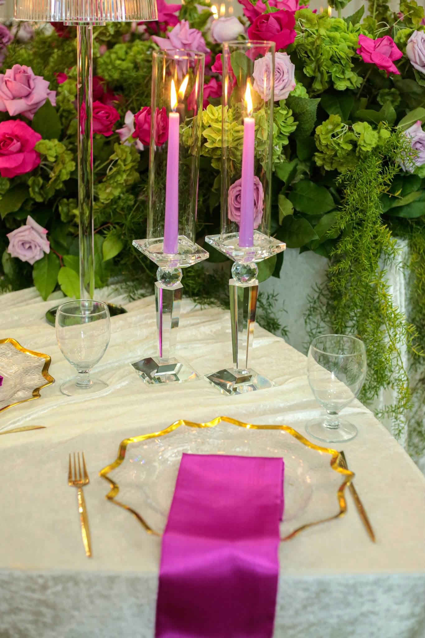 Elegant place setting featuring gold rim ruffled glass charger, satin purple napkin, modern gold flatware, and crystal candlestick holders