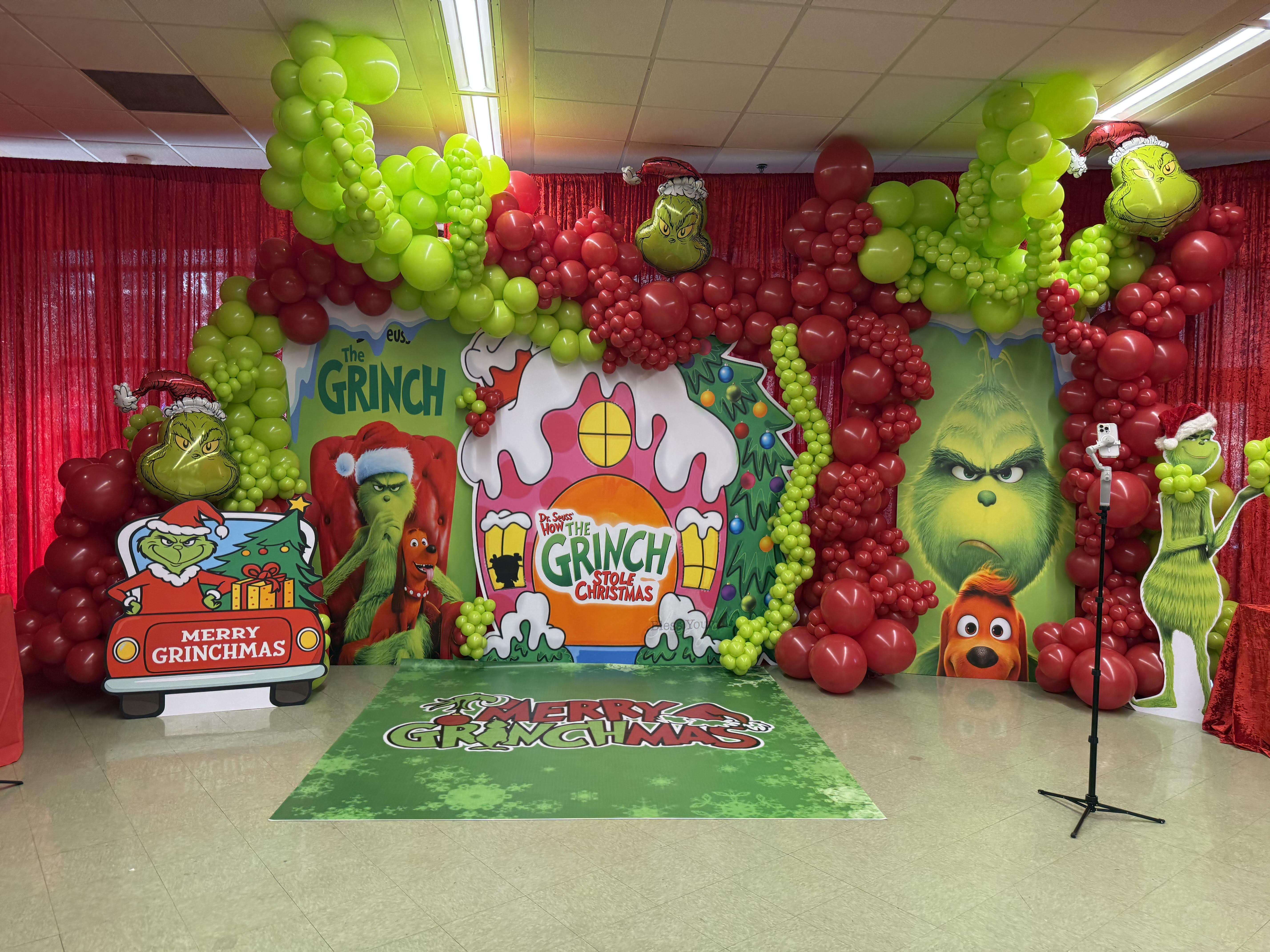 Whimsical Grinch-themed Christmas installation featuring vibrant red and lime green balloon garlands, custom character cutouts, and festive printed floor wrap
