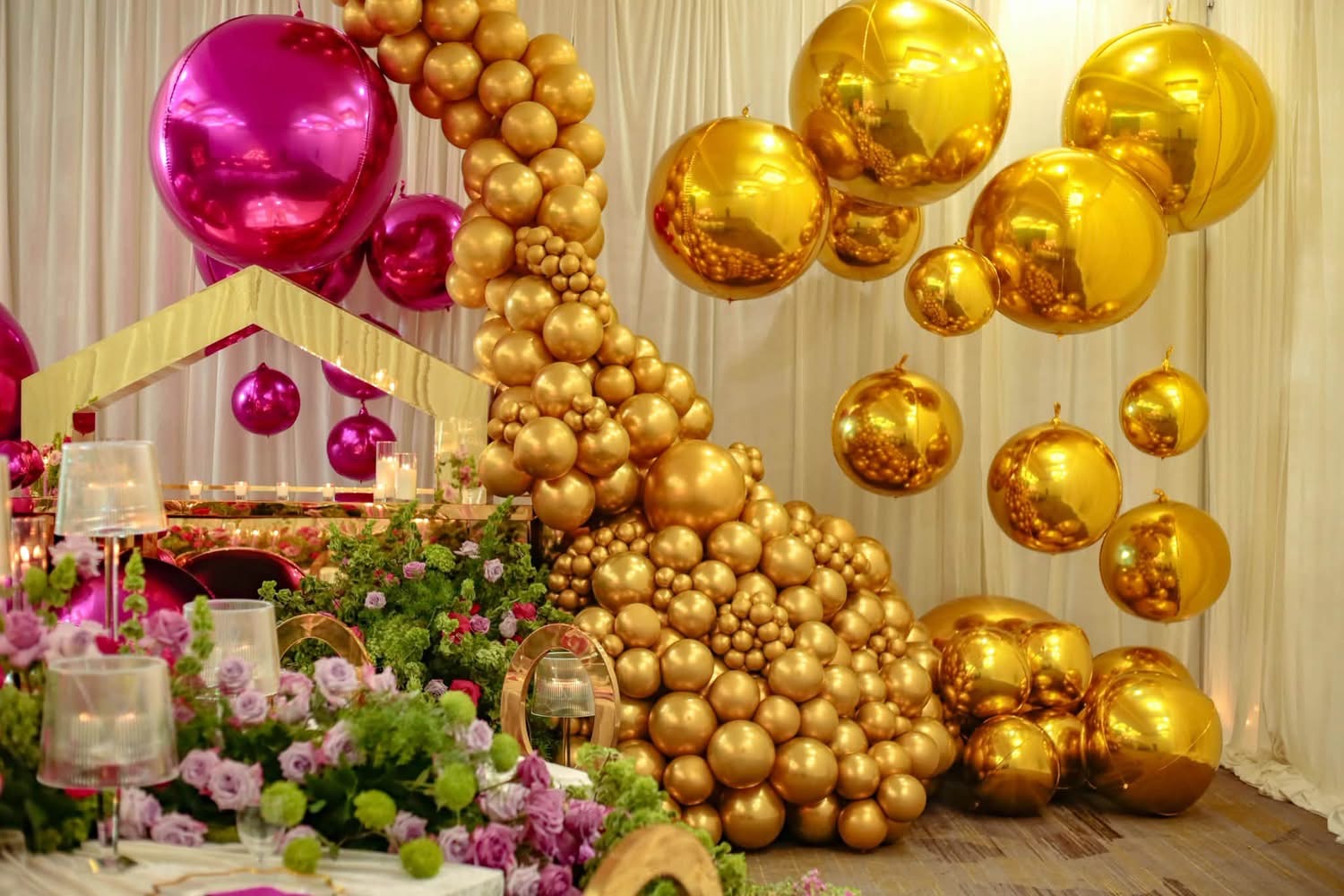 Sculptural metallic gold balloon cascade with floating reflective gold and magenta chrome spheres and ambient candlelight