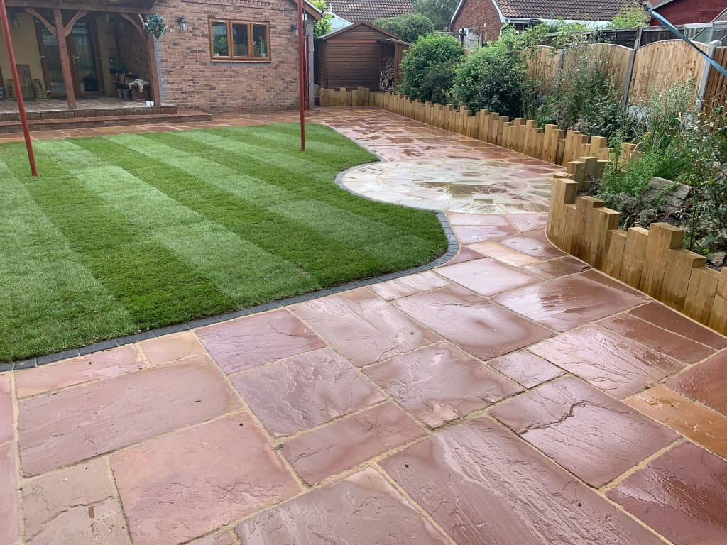Striped new lawn with curved charcoal edging, sandstone circle feature patio, and vertical sleeper border
