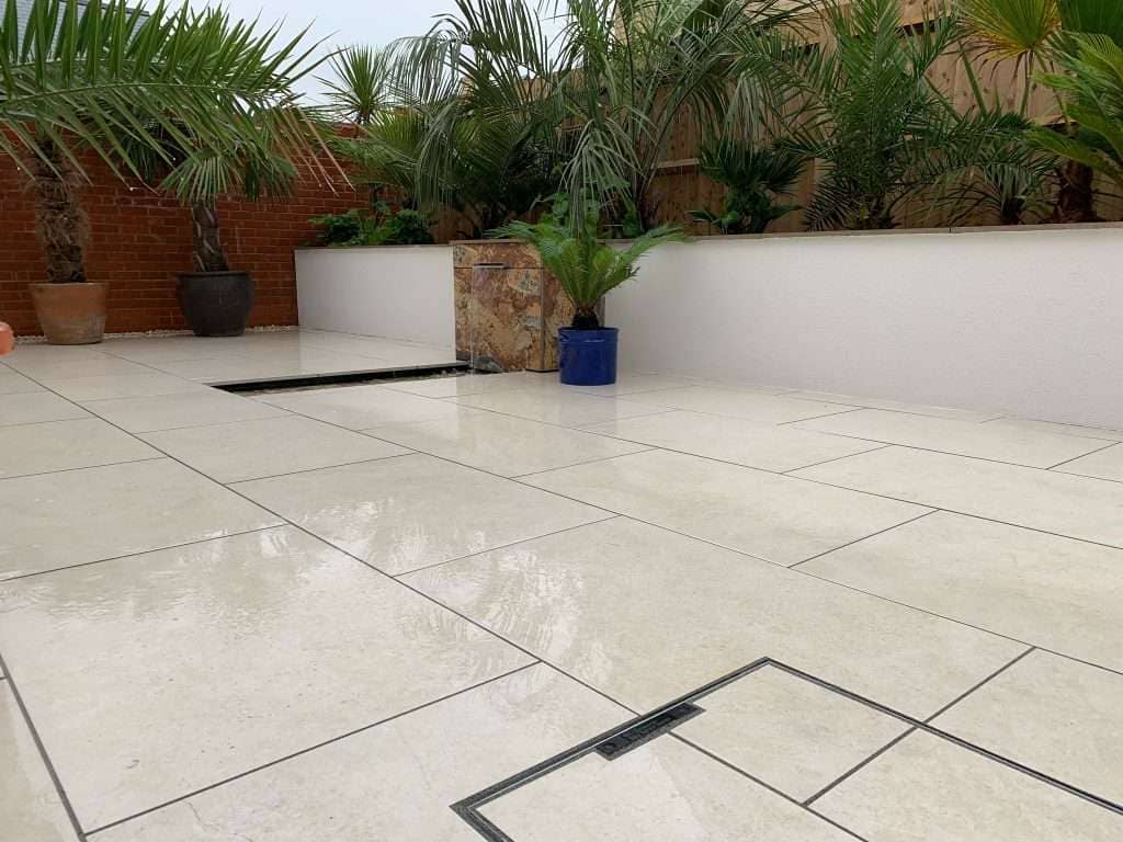 Cream porcelain patio tiles with raised white rendered wall planter filled with tropical plants