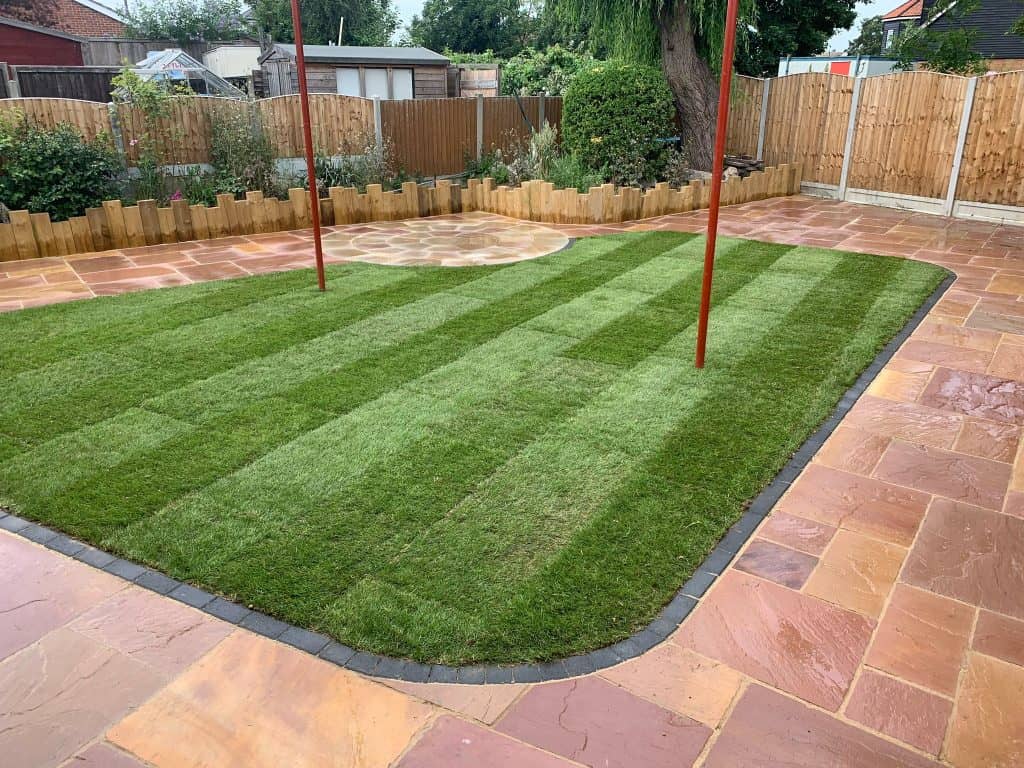 Newly turf lawn with curved sandstone paving edging and vertical sleeper retaining wall in Basildon