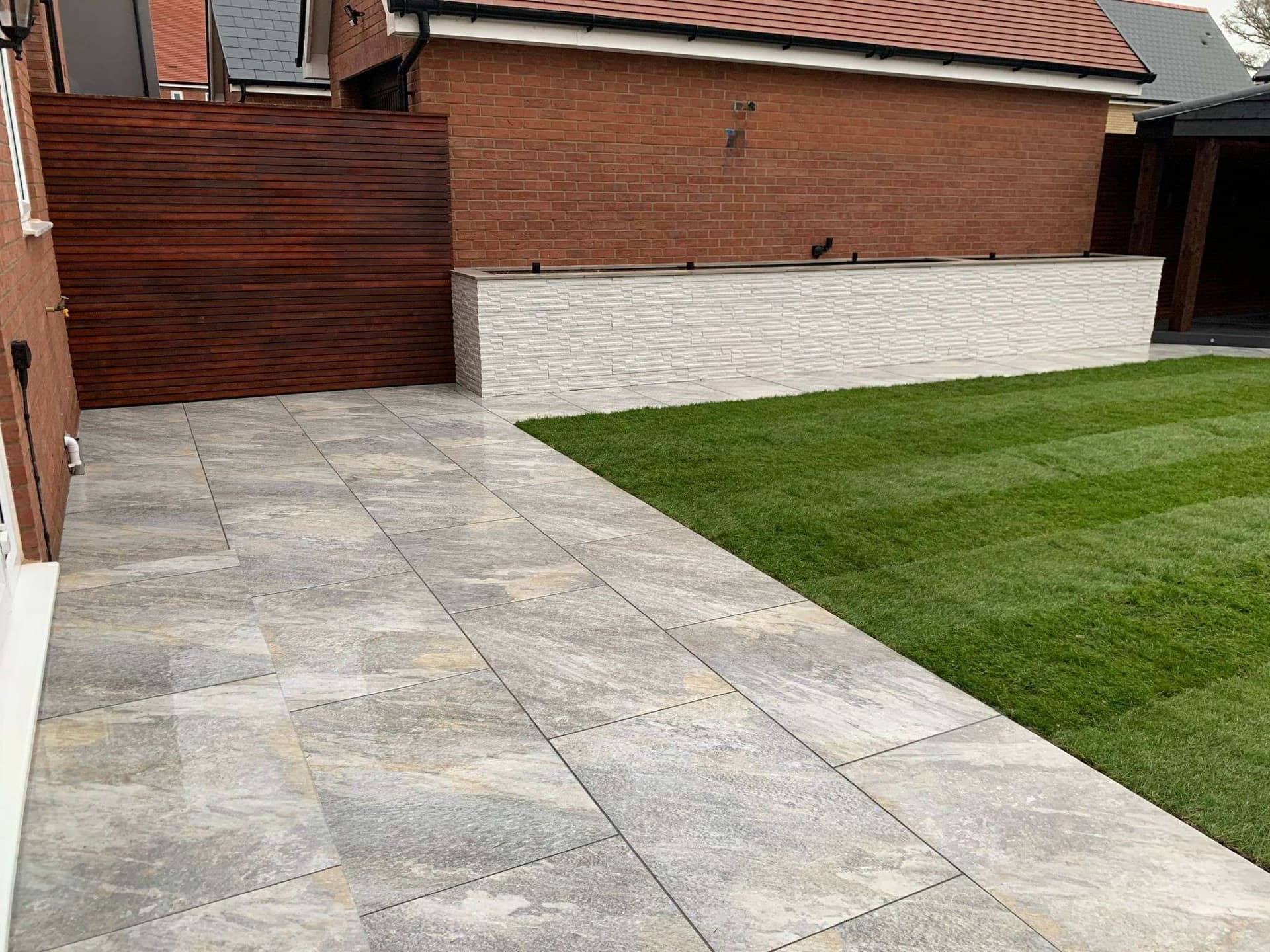 Porcelain patio paving installation with immaculate striped lawn turfing in Billericay