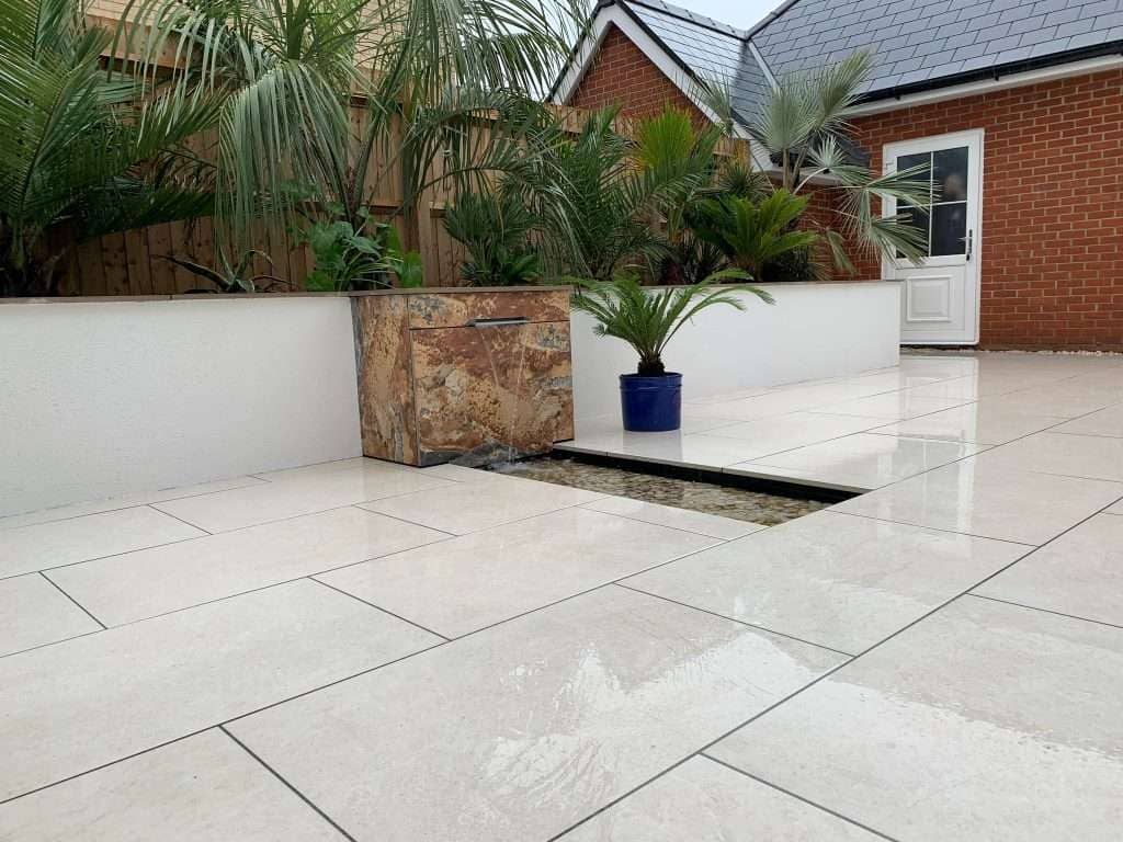 Wide angle view of cream porcelain paving, stone water feature and raised beds in Rayleigh