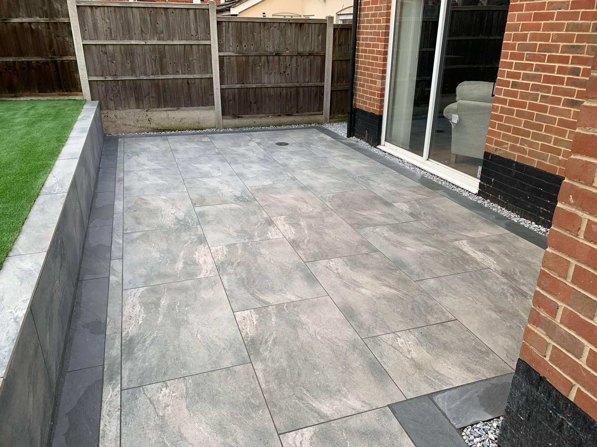 Porcelain patio paving with contrasting charcoal border edging and raised artificial lawn