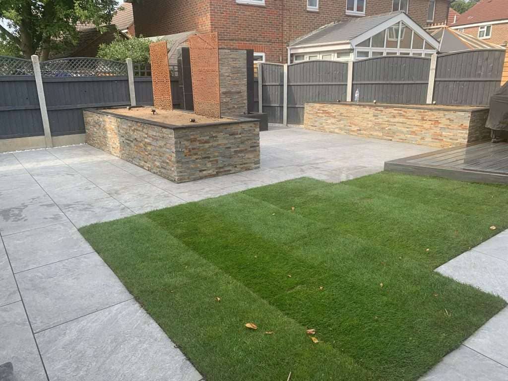 Freshly laid lawn turf next to grey porcelain patio slabs and stone raised planter beds