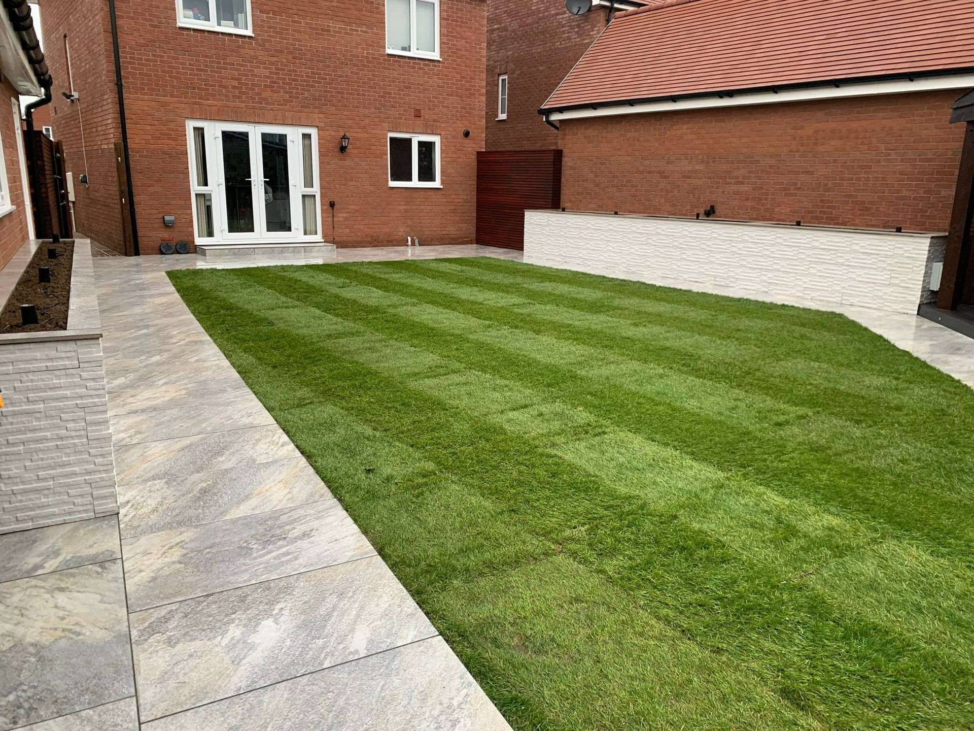 Clean striped lawn turf and porcelain paving layout in new build garden