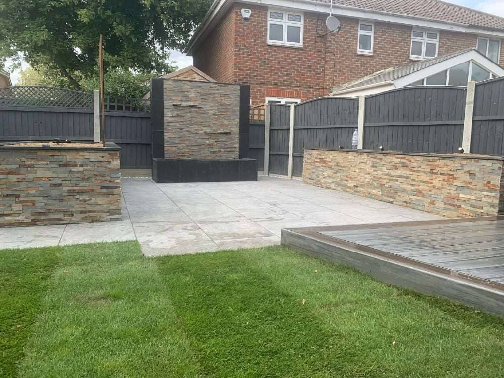 Full garden overview showing grey porcelain patio, fresh lawn turf, composite deck and stone water feature