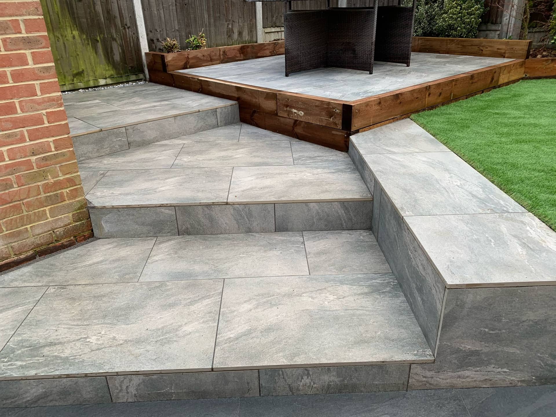Raised patio terrace with porcelain steps and artificial grass lawn in Billericay