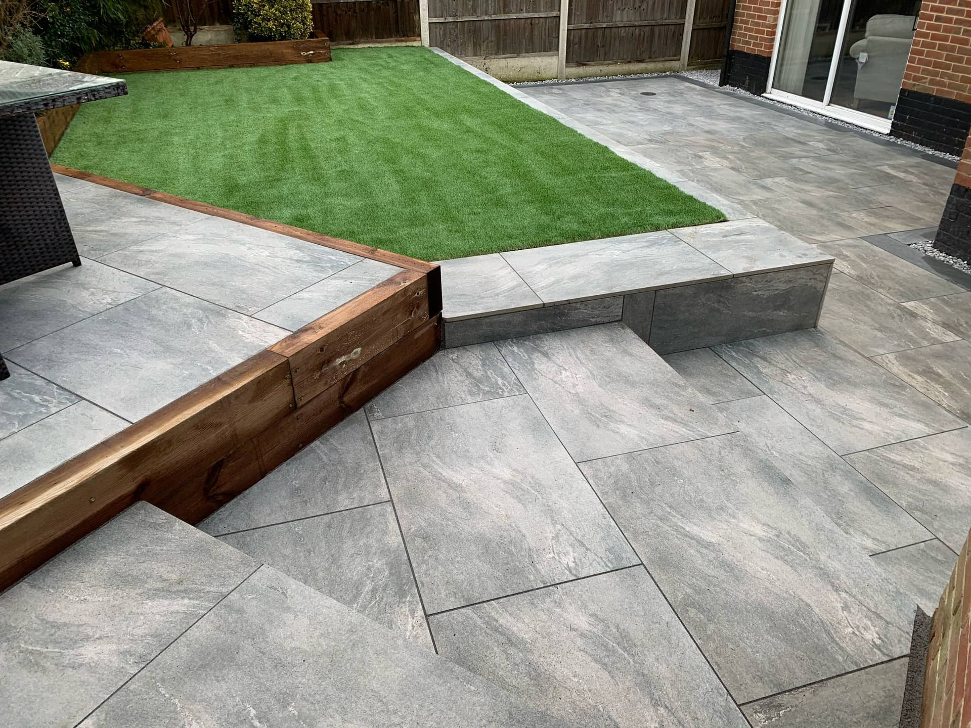 Raised timber railway sleeper planter bed framing the upper artificial lawn tier