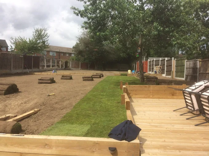 Complete garden landscaping project showing prepared ground, new turf lawn, timber decking and raised beds under construction