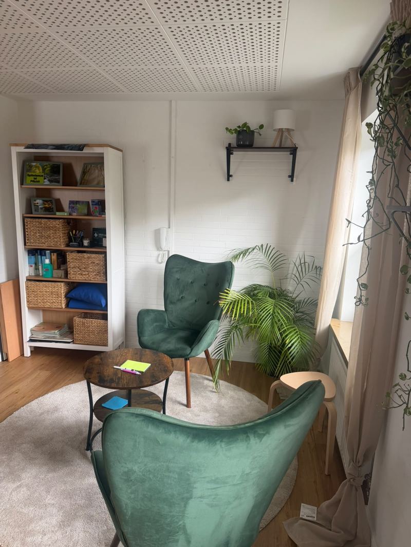 Gesprächsraum in der Praxis Lüneburg mit zwei grünen Sesseln, rundem Tisch, Palme und Bücherregal