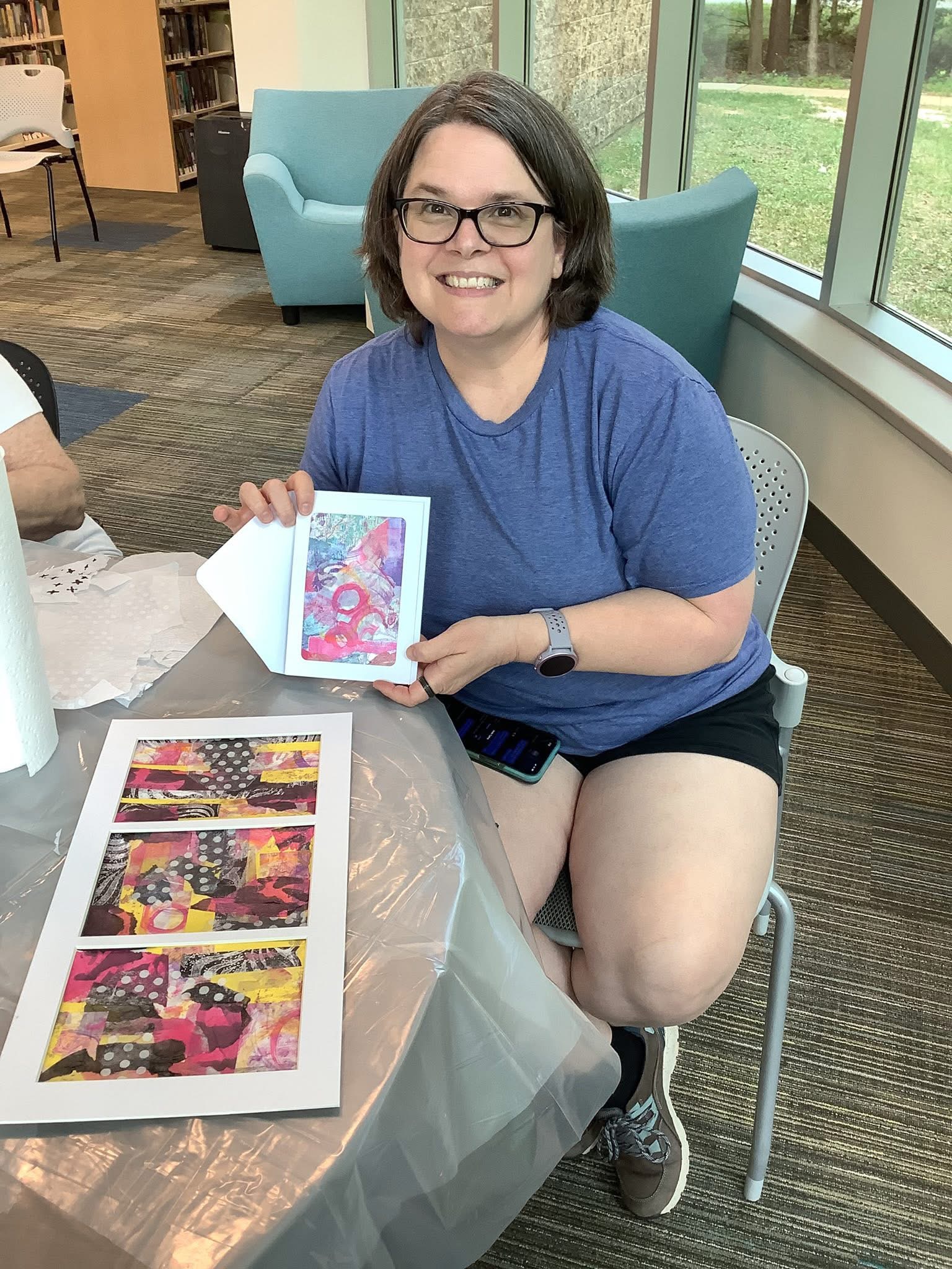 Laurie McAleenan smiling and presenting colorful handmade mixed-media art cards and prints