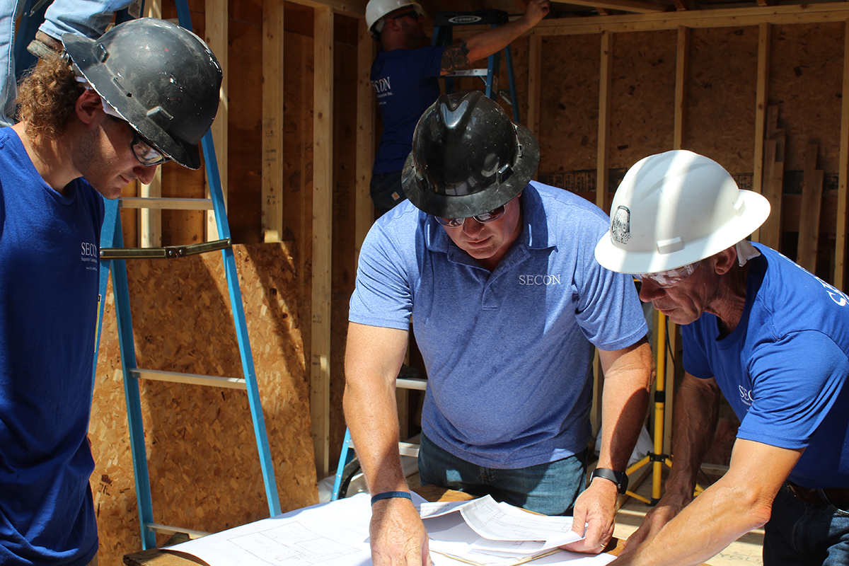 SECON team reviewing architectural blueprints on a job site wearing branded apparel