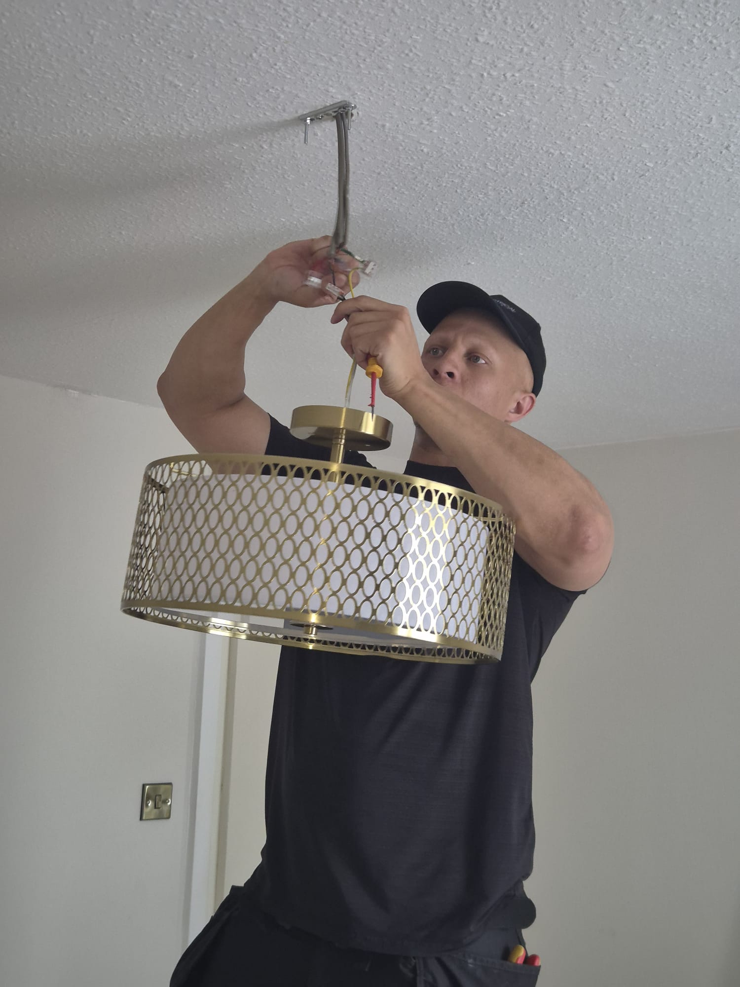 Electrician installing and wiring a designer brass drum pendant light fitting to ceiling rose