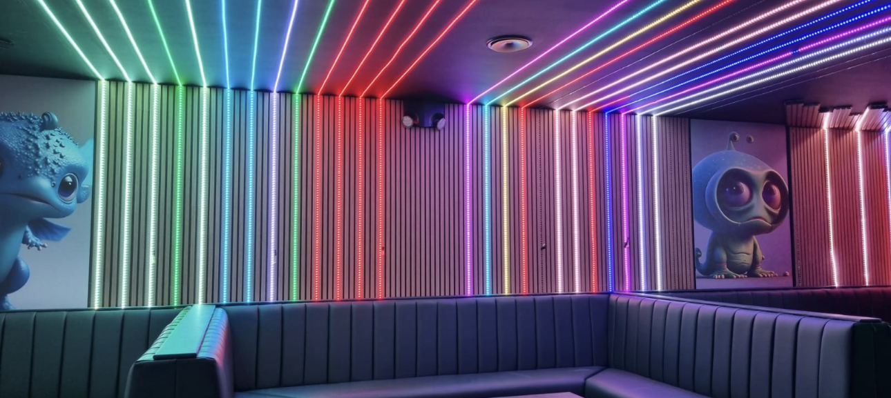 Custom multicoloured RGB LED ceiling and wall channel feature lighting installed along timber acoustic slat panels