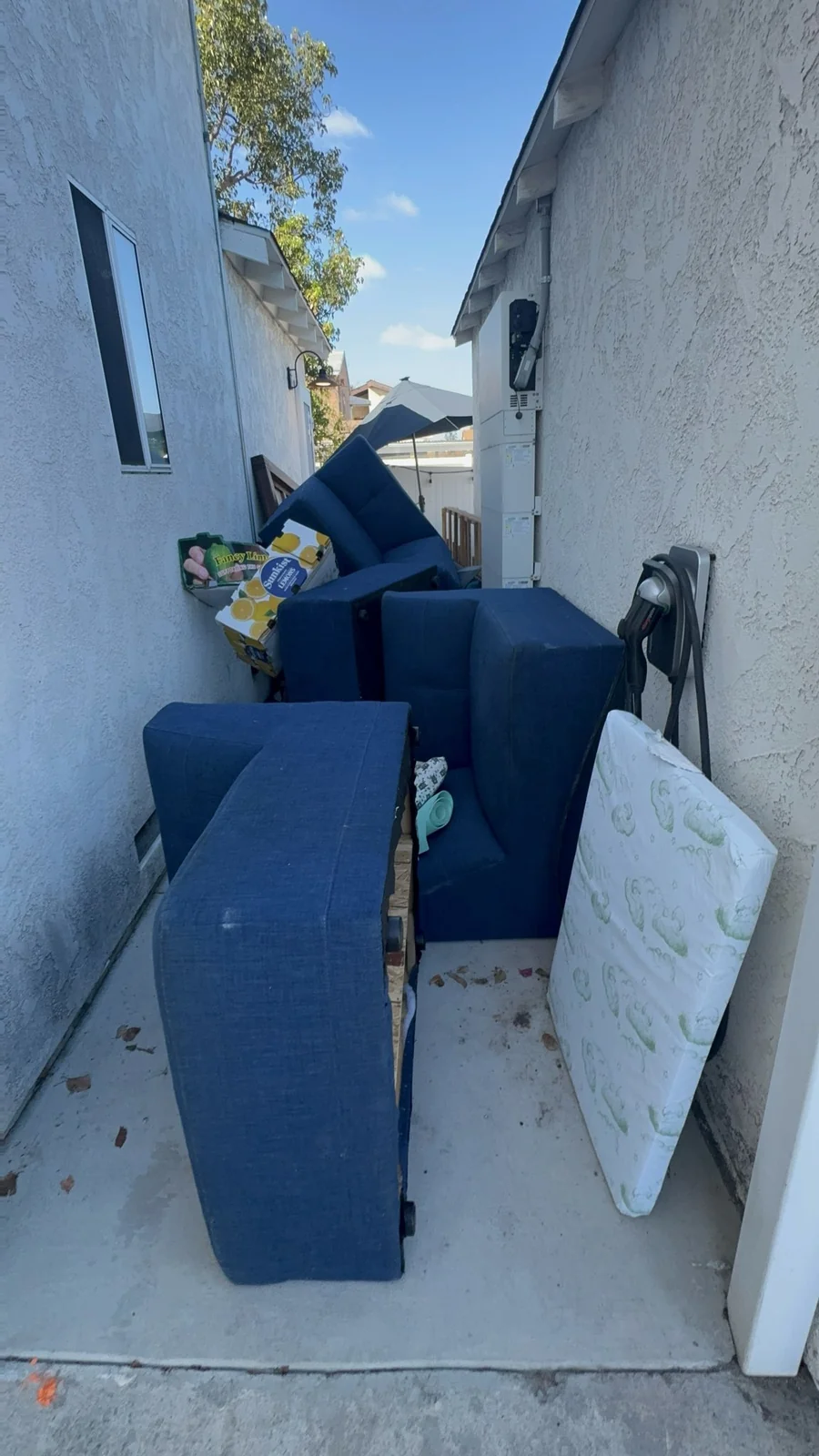 Sectional sofa pieces, furniture, and trash awaiting removal in a City Heights side walkway.