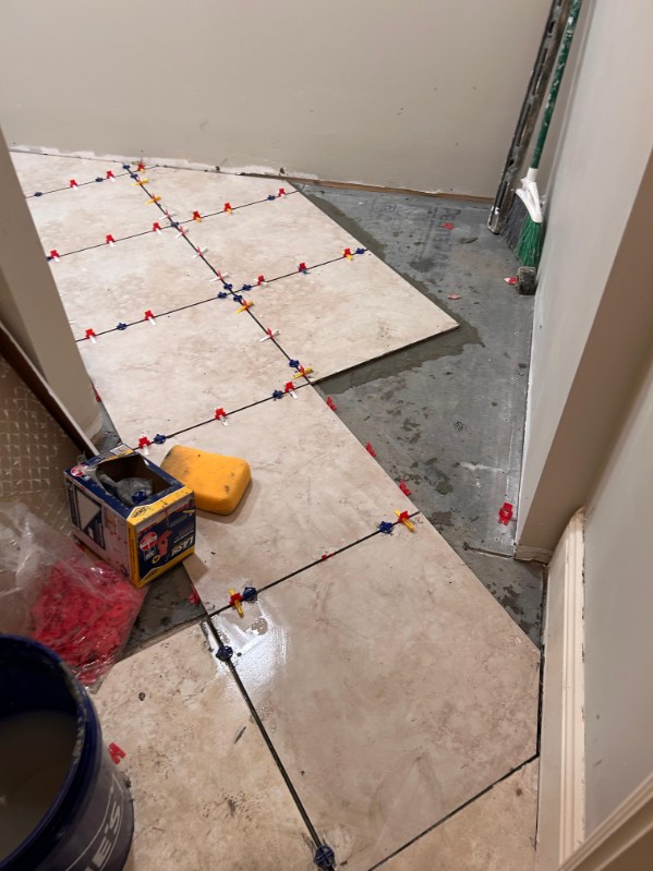 Porcelain floor tile installation in progress with red and yellow leveling clips