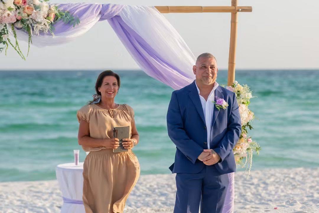 Marlene Cabrera Culpepper officiating with a groom on the beach under a lavender-draped arbor