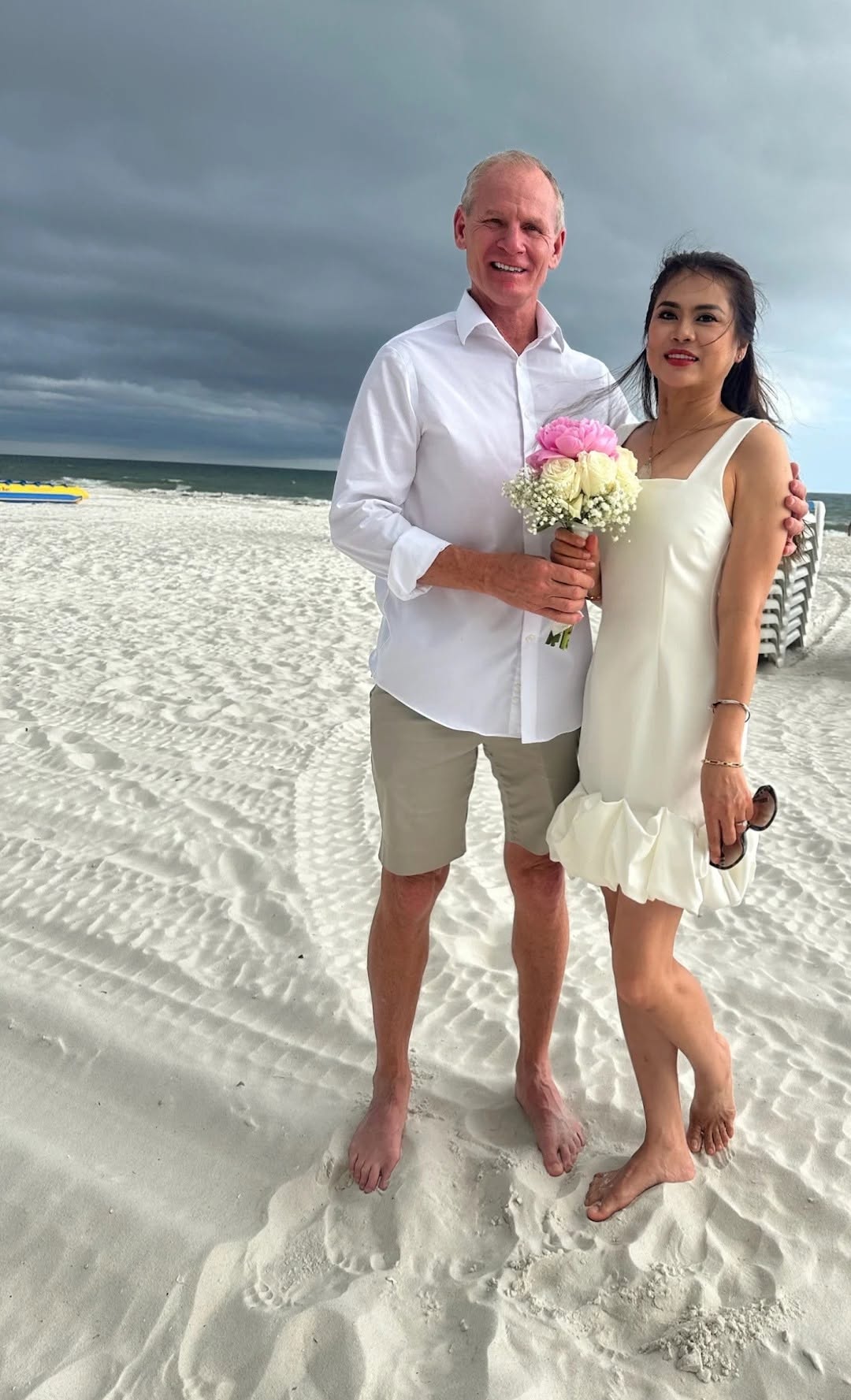 Happy newlywed couple barefoot on the sugar-white sand holding a bridal bouquet