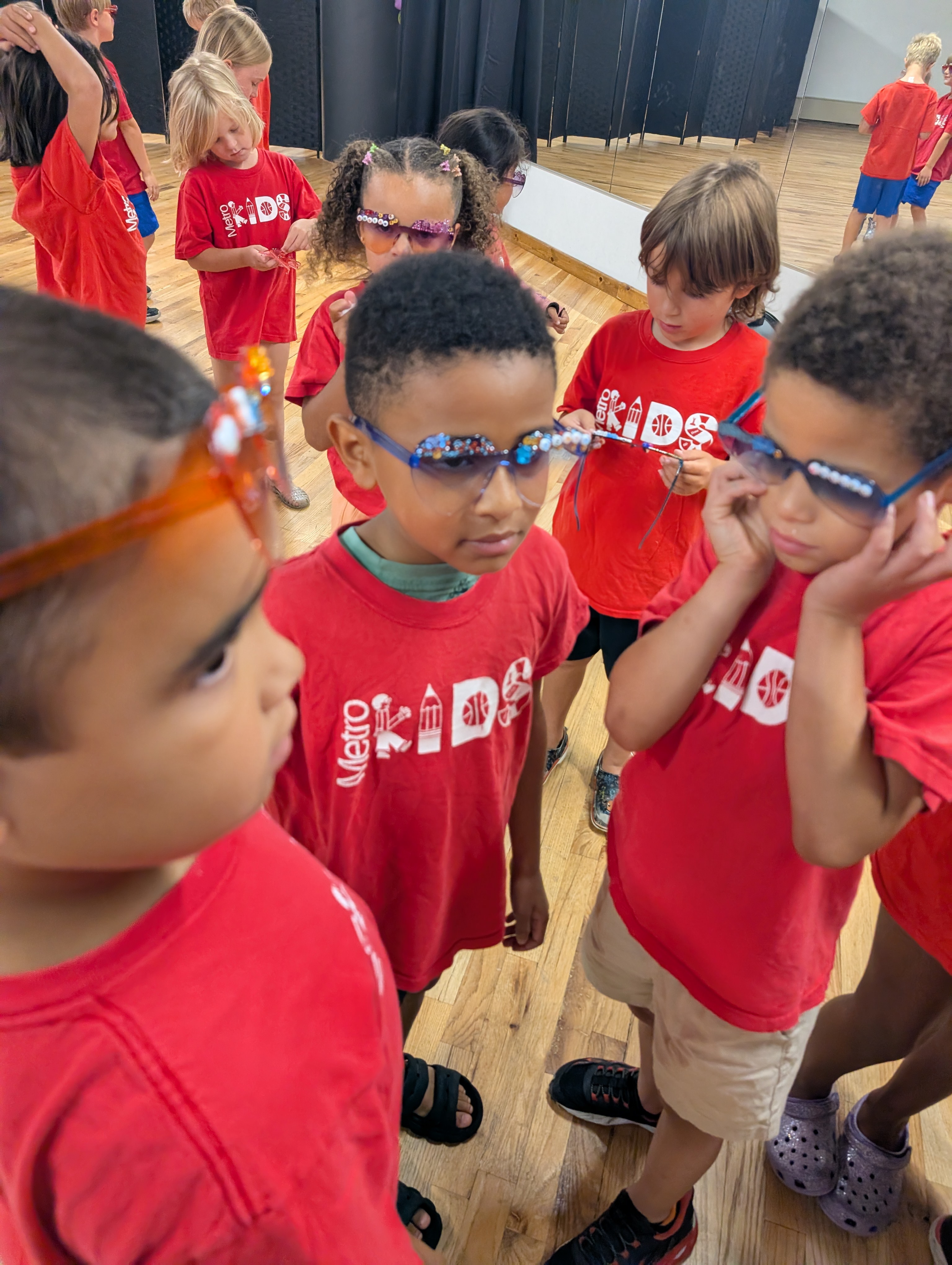 Kids in red Metro Kids shirts checking out and trying on their custom jeweled sunglasses