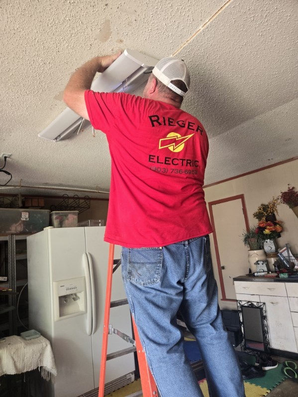 Rieger Electric electrician on a ladder replacing a ceiling light fixture