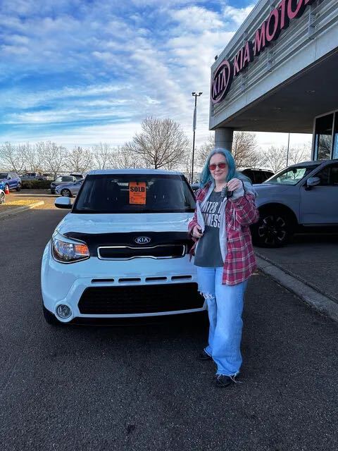 Happy customer holding keys in front of white Kia at dealership