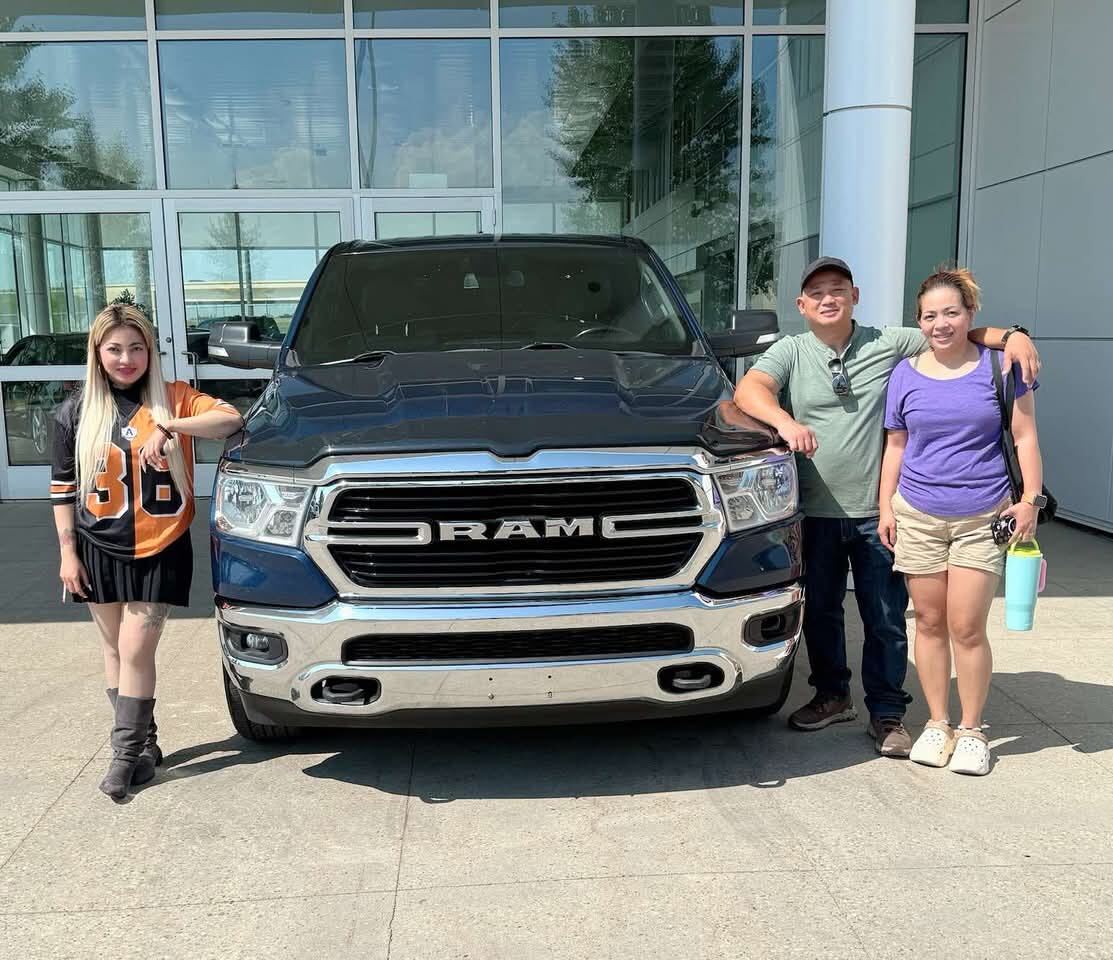 Family of three smiling in front of new dark blue RAM pickup truck