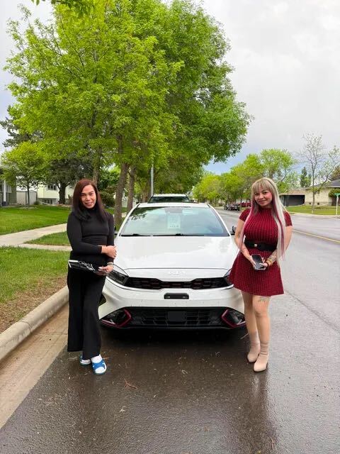 Two happy buyers standing in front of new white Kia car