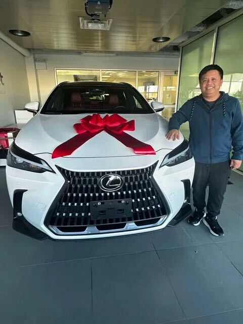 Smiling client taking delivery of white Lexus with big red bow
