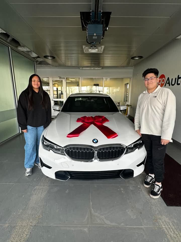 Smiling clients in showroom with white BMW featuring red bow