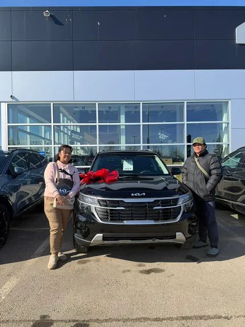 Two clients taking delivery of black Kia with red bow