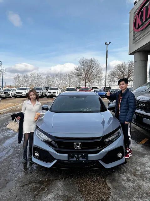 Couple smiling in front of new grey sedan