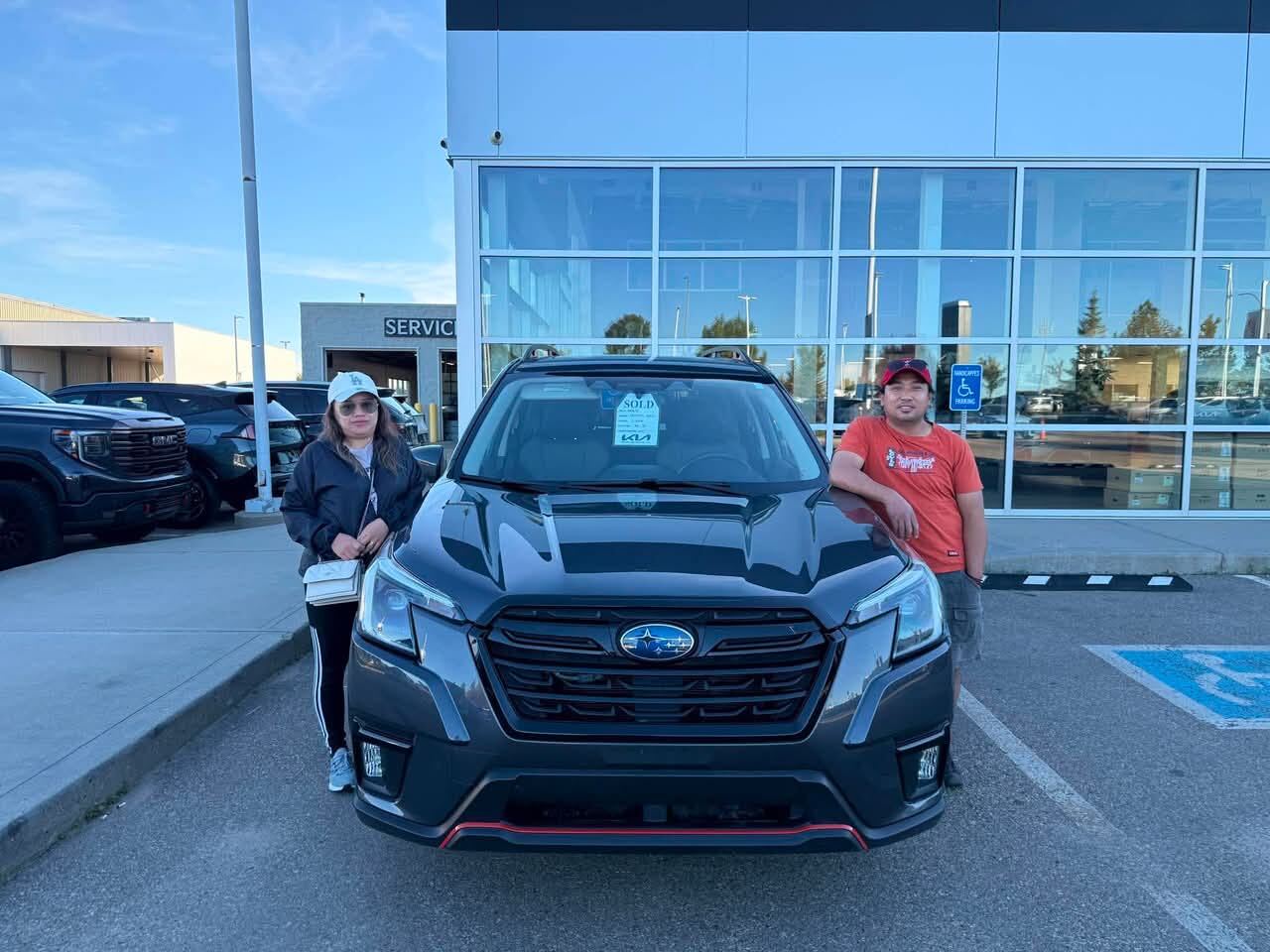 Proud couple standing beside their dark grey Subaru SUV
