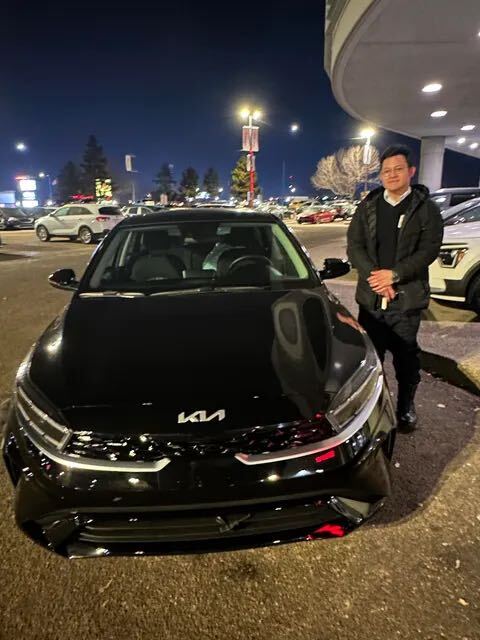 Client smiling next to new black Kia sedan at dealership