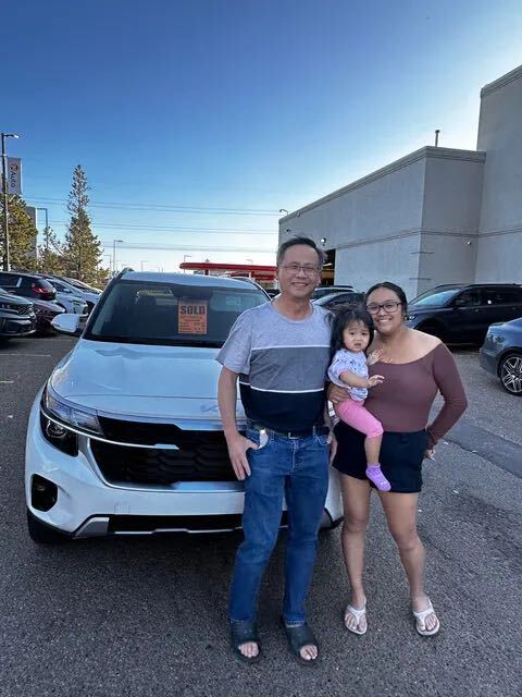 Happy family with baby in front of white Kia SUV with sold sign