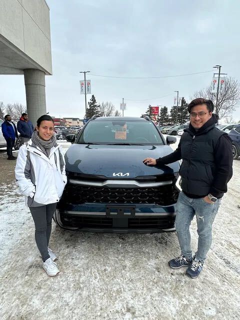 Couple standing beside new dark blue Kia SUV in winter