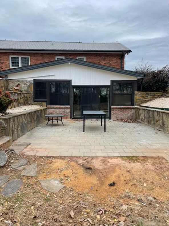 Rear elevation of home addition with sliding glass doors, vertical siding, brick foundation tie-in, and stone courtyard patio